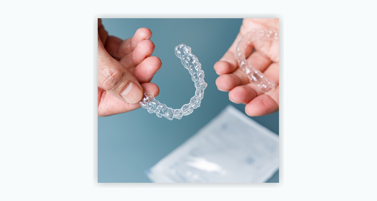 SureSmile clear aligner tray held in hand against a blue background